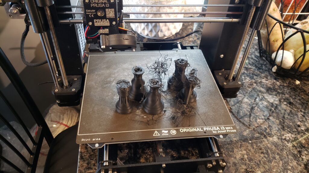 A bunch of half-printed chess pieces, damaged by the print nozzle, full of wiry filament printed in mid-air