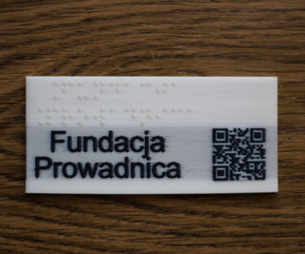 PLA, white plate with black inscription Fundacja Prowadnica, white Braille inscription and QR code